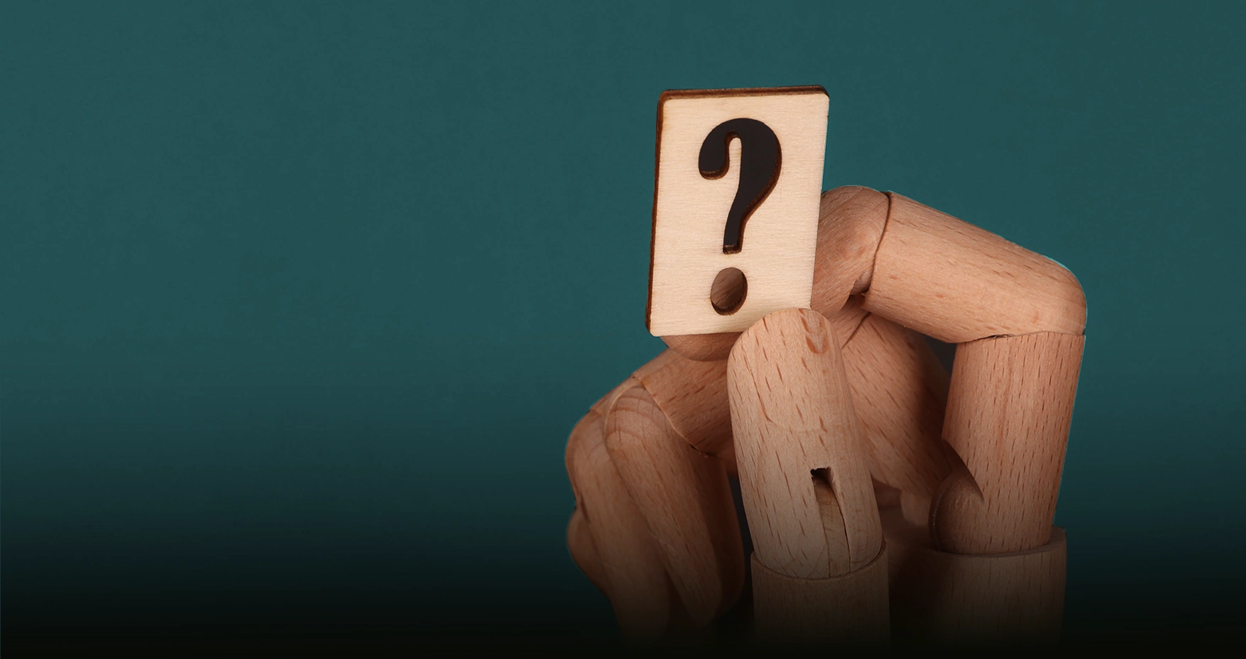 A wooden artist mannequin holding a question-mark tile against a teal background.